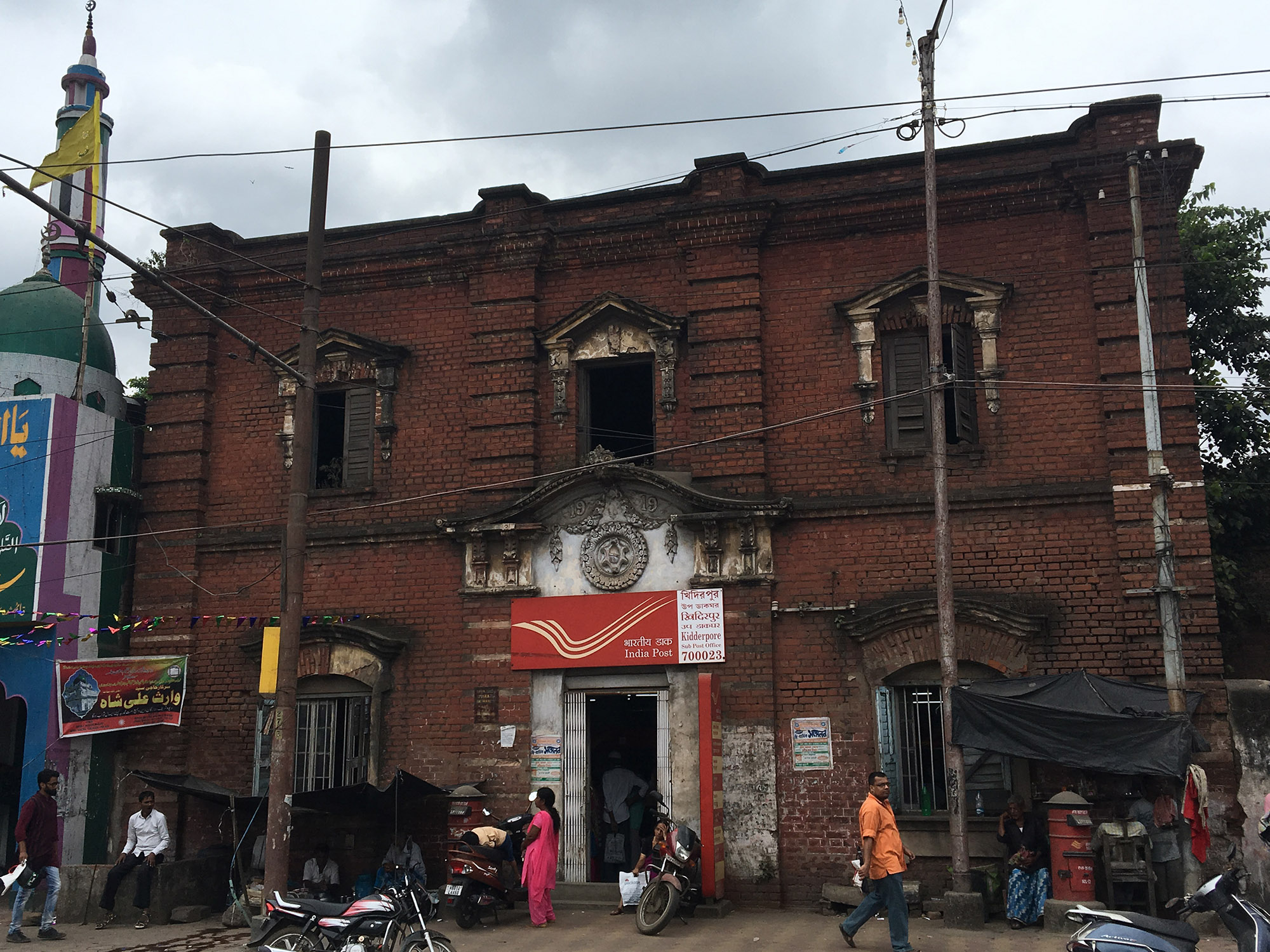 A dilapidated mansion-style building from 1919 that has been converted into a post office; detailed Indo-Corinthian pilaster work and wooden Venetian windows can be seen on its facade [Neha Banka/Al Jazeera]