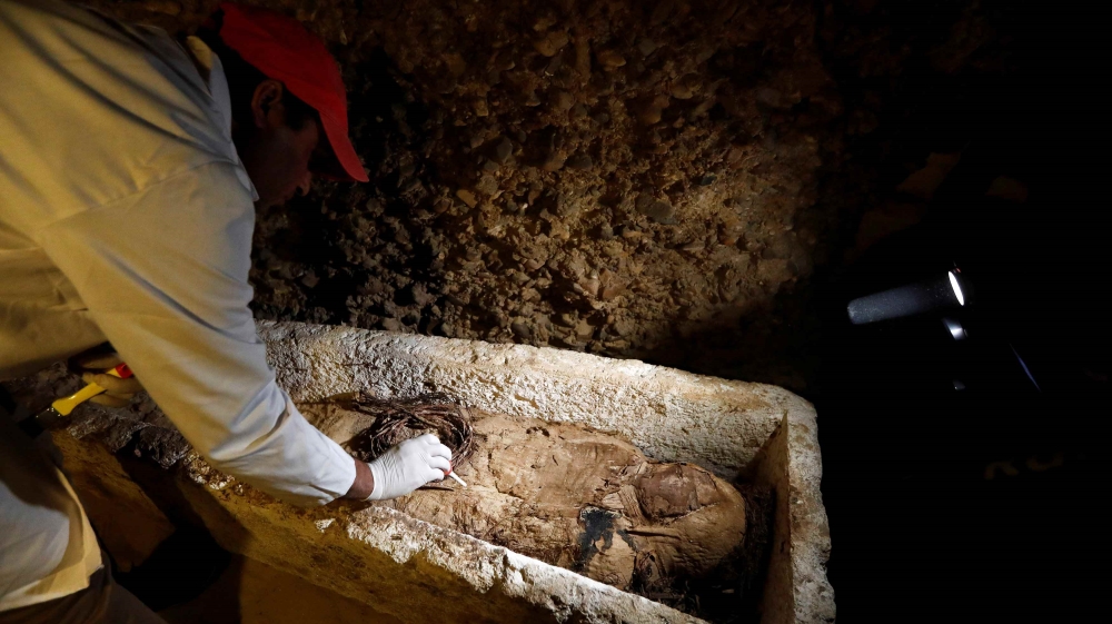 An Egyptian archaeologist examines a mummy in a coffin [Amr Abdallah Dalsh/Reuters]
