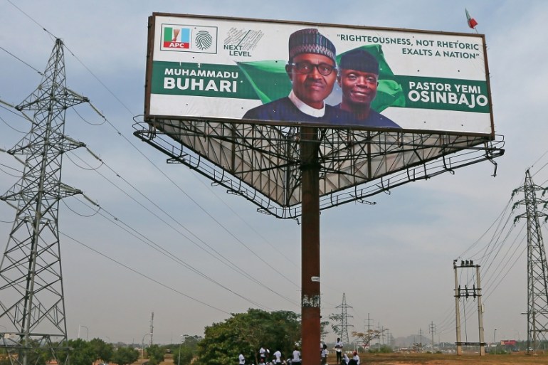 People sit under an election campaign billboard in Abuja
