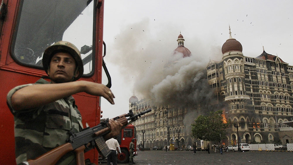 An Indian soldier takes cover as the Taj Mahal hotel burns during gun battle between Indian military and rebels inside the hotel in Mumbai, India. [David Guttenfelder, File/The Associated Press]