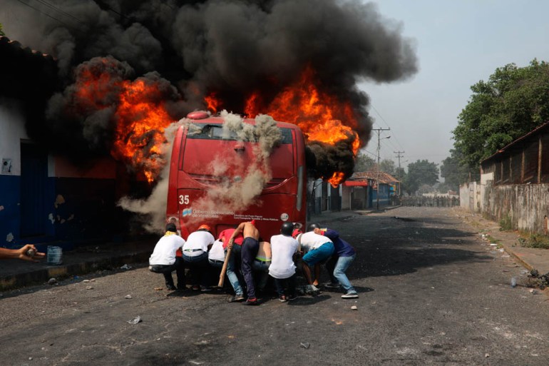 Demonstrators push a bus that was torched during clashes with the Bolivarian National Guard in Urena, Venezuela, near the border with Colombia, Saturday, Feb. 23, 2019. Venezuela''s National Guard fire