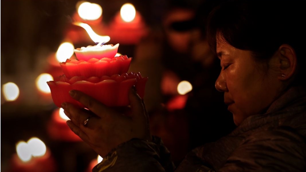 A woman holding a flower-shaped candle prays on the first day of the Chinese Lunar New Year at the Tanzhe temple in Beijing's Mentougou District [Andy Wong/The Associated Press]