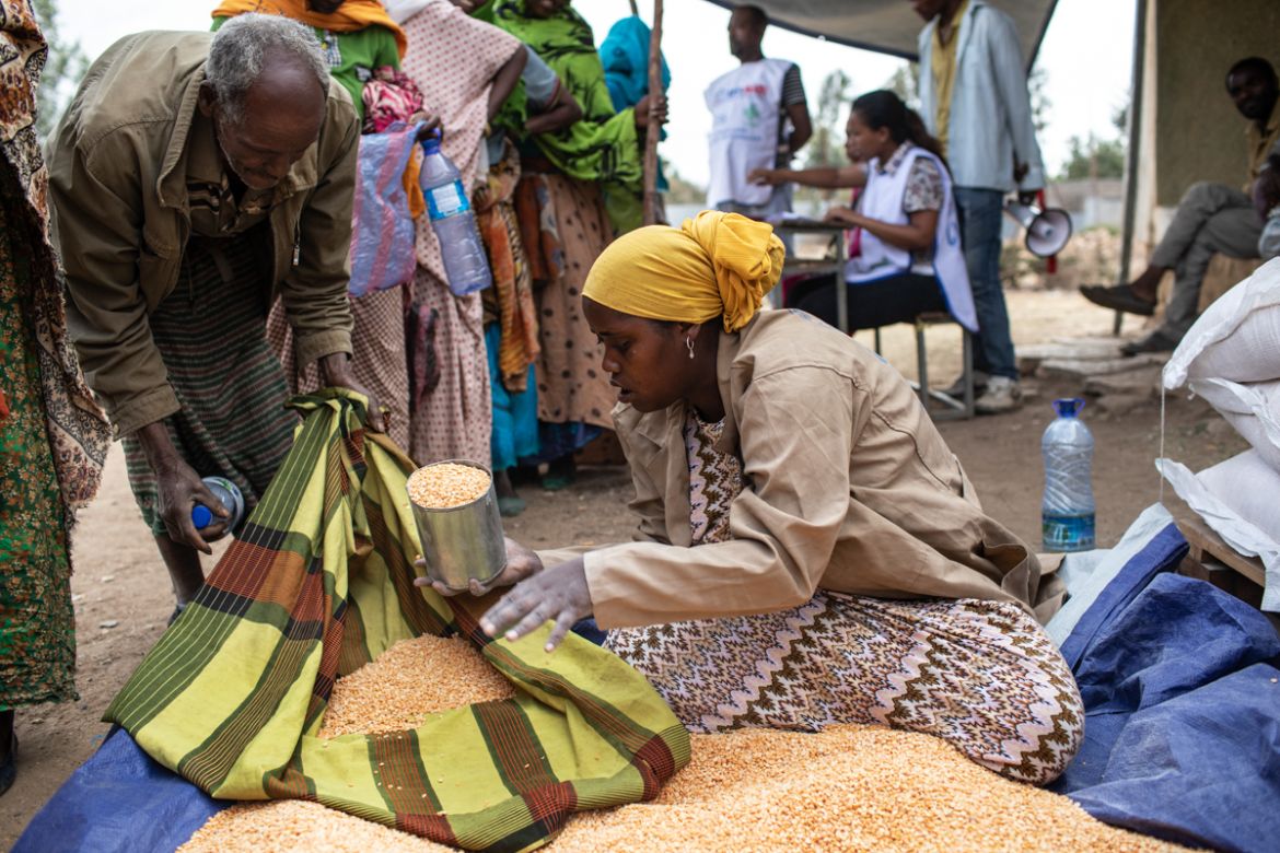 A woman dishes out a ration of yellow split peas to a man during a distribution of USAID food in Kersa district, Oromia Region, on February 9, 2018. Families identified for support receive rations of