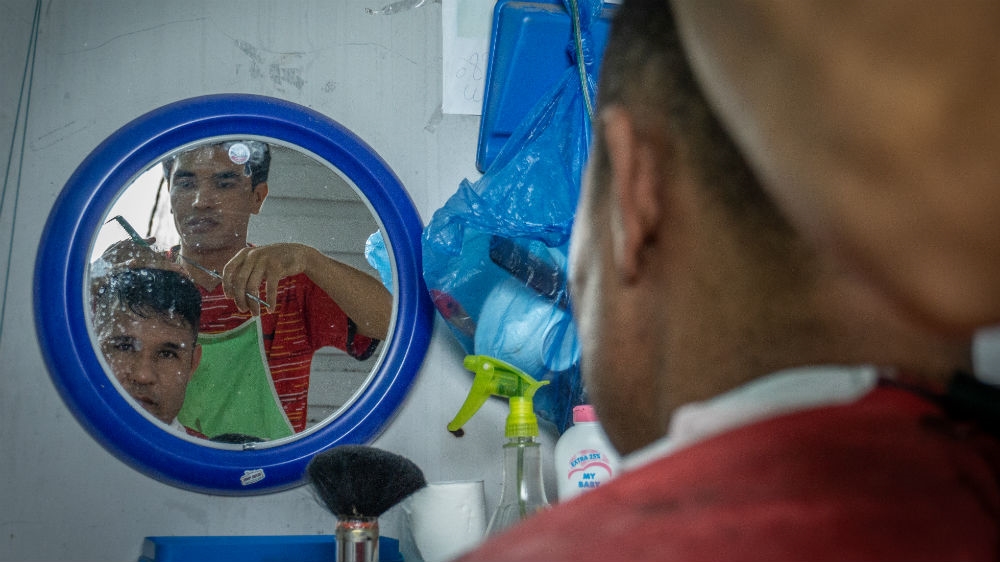 Muhammad Amiri has his hair cut at a barbershop in the refugee shelter in Makassar, Indonesia [Ian Morse/Al Jazeera]