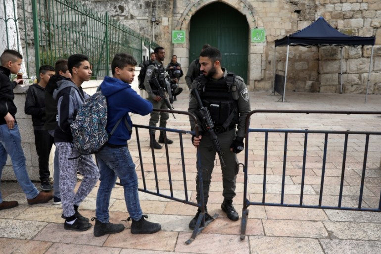 Kids stand by a barrier as Israeli border police guard at an entrance door leading to the compound housing al-Aqsa Mosque in Jerusalem''s Old City