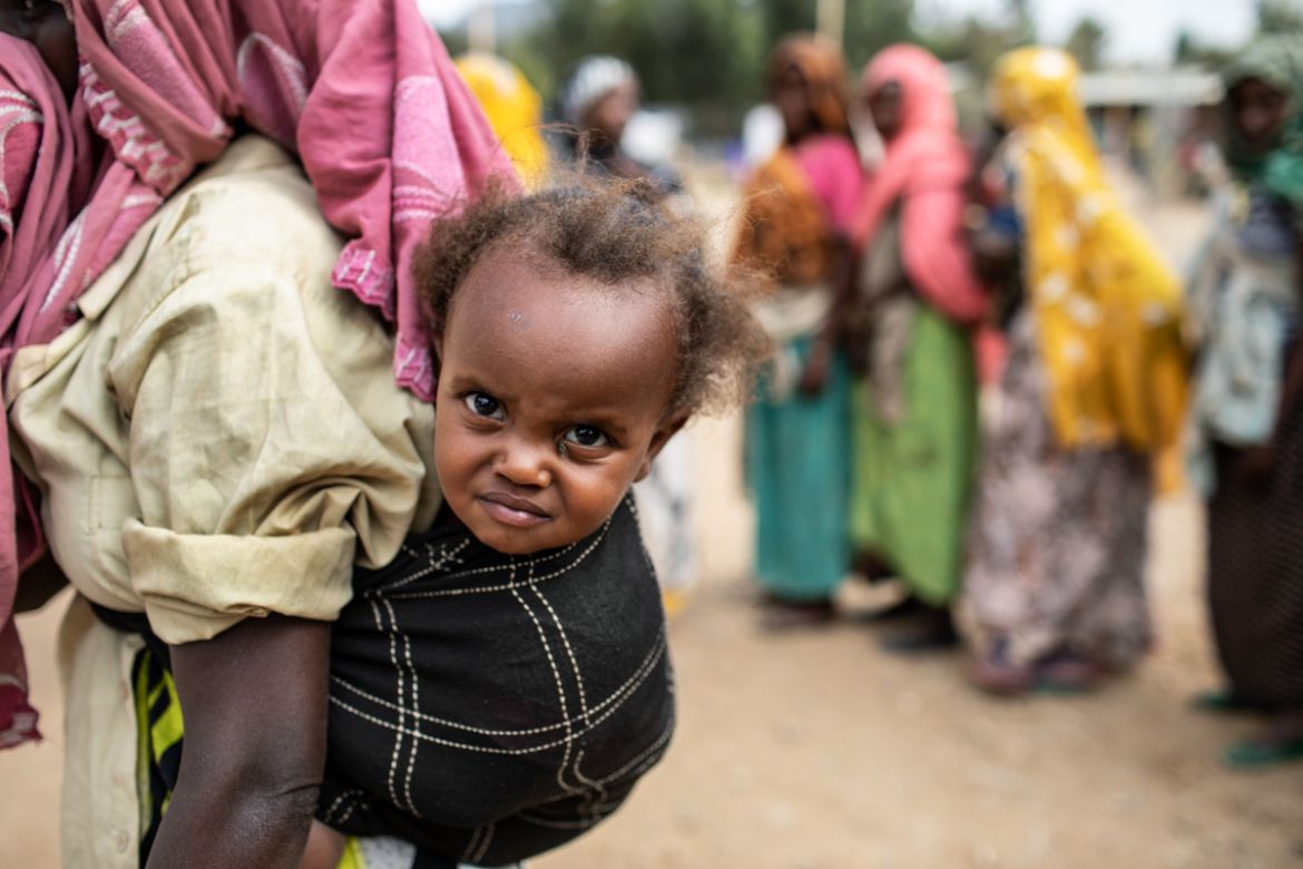 A woman carries an infant on her back during a distribution of USAID food in Kersa district, Oromia Region, on February 9, 2018. According to the World Health Organization, droughts in developing coun