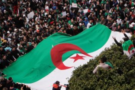 A demonstrator gestures from atop of a tree as others carry a giant national flag during a protest calling on President Abdelaziz Bouteflika to quit, in Algiers