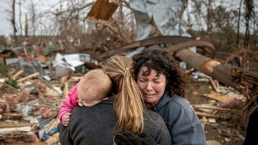 Carol Dean, (right), cries while embraced by Megan Anderson and her 18-month-old daughter Madilyn, as Dean sifts through the debris of the home she shared with her husband, David Wayne Dean, who died when a tornado destroyed the house in Beauregard [David Goldman/AP Photo]