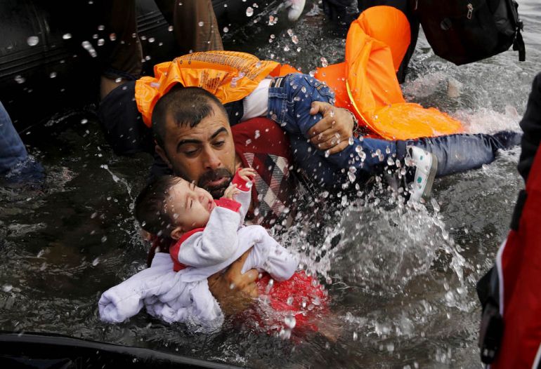 A Syrian refugee holds onto his children as he struggles to walk off a dinghy on the Greek island of Lesbos, after crossing a part of the Aegean Sea from Turkey to Lesbos September 24, 2015. REUTERS/Y