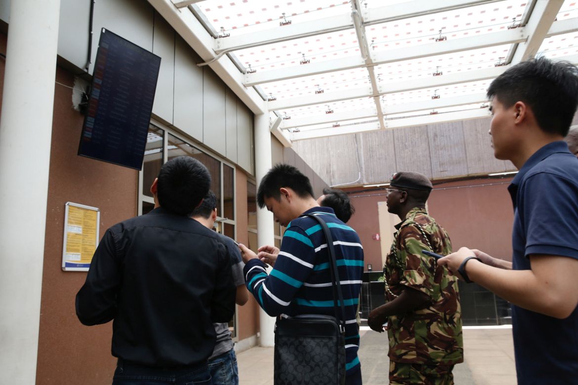 Chinese people and a Kenyan military officer use their mobile phones near the flight information board displaying the details of Ethiopian Airlines Flight ET 302, where their colleagues were onboard a