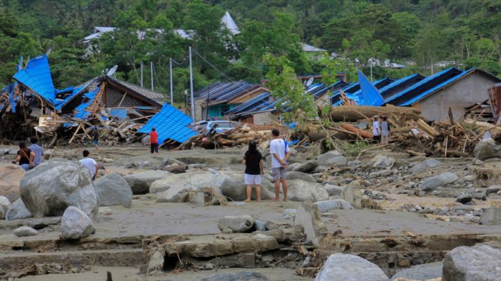 People stand as they look at damaged houses after a flash flood in Sentani, Papua