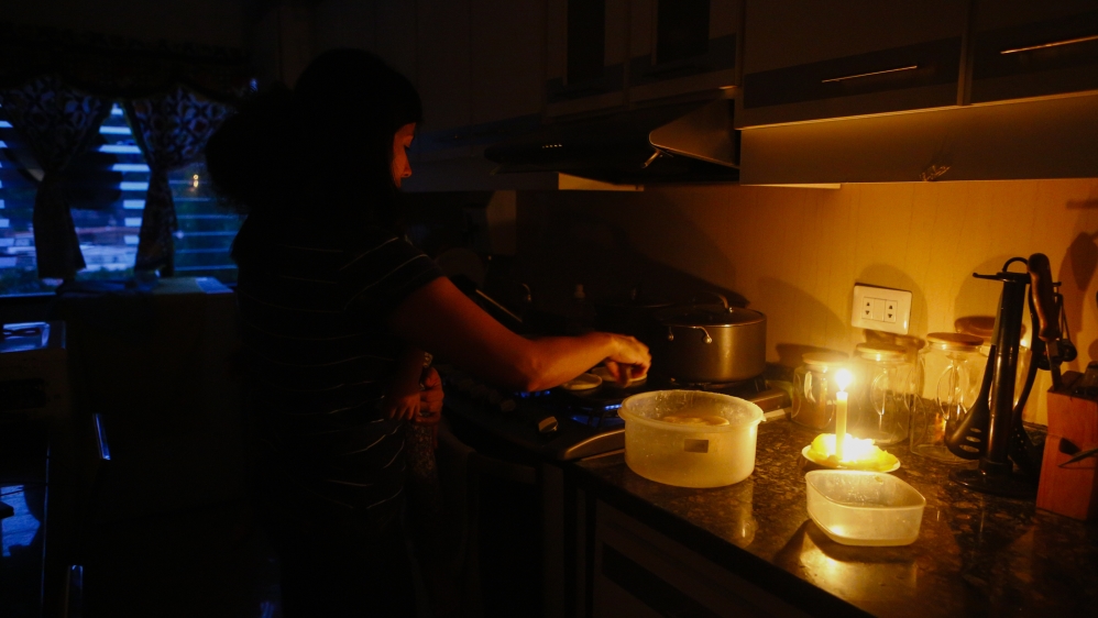 A woman cooks dinner at her house with the help of a candle during blackouts in Venezuela [Eva Marie Uzcategui/Getty Images]