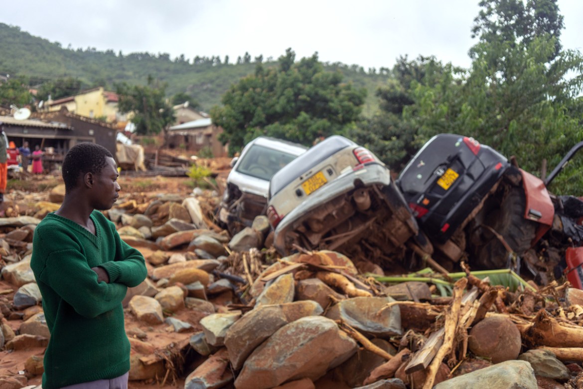 A man stands next to the wreckage a vehicles washed away on March 18, 2019 in Chimanimani, eastern Zimbabwe, after the area was hit by the cyclone Idai. - A cyclone that ripped across Mozambique and