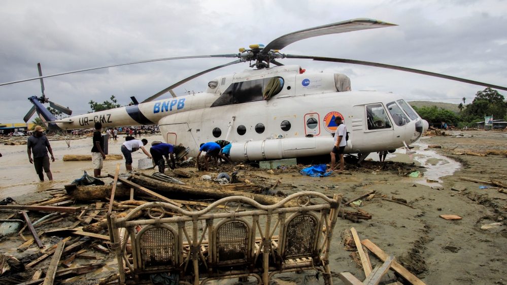 People stand near a helicopter that was moved by flash floods in Sentani, Papua [Antara Foto/Gusti Tanati/Reuters]