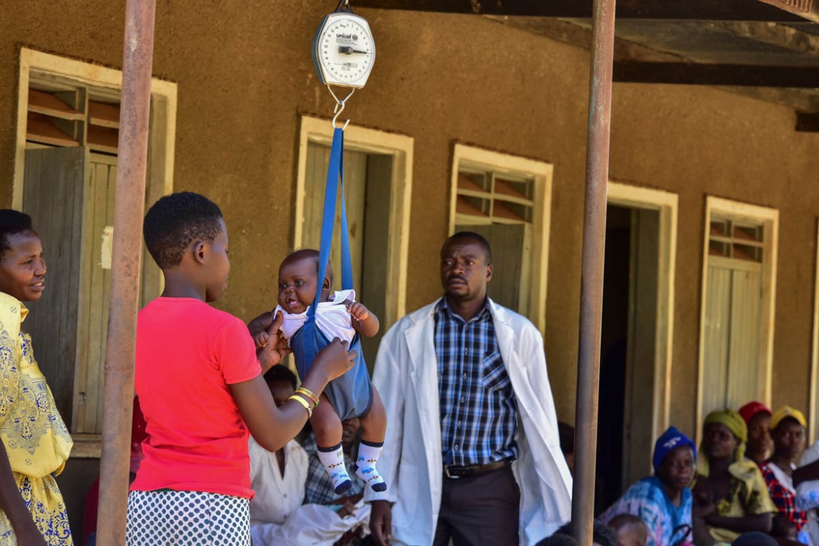 A mother weighs her baby at Kibibi Health center in Budondo Sub county Jinja District, as Musomba Joshua (R) watches, Musomba is an enrolled comprehensive Nurse at the facility.