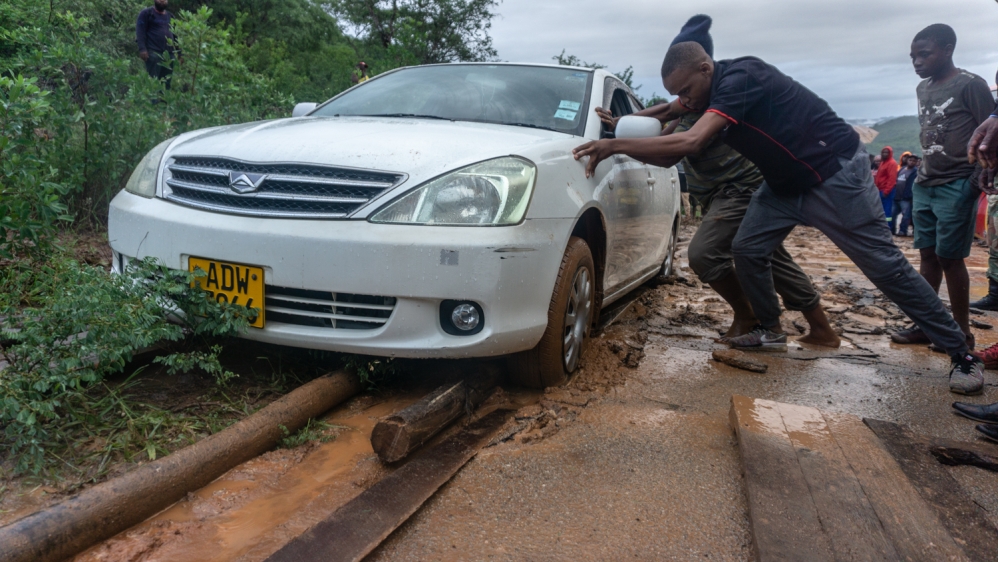 Volunteers try to push a car stuck in the broken muddy road in Chipinge, Zimbabwe [Tendai Marima/Al Jazeera]