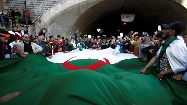 People carry a giant national flag as they protest over President Abdelaziz Bouteflika''s decision to postpone elections and extend his fourth term in office, in Algiers