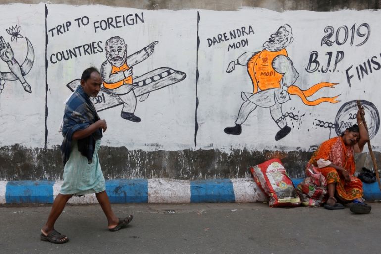 A man walks past a woman who sits by a wall with graffiti that mocks Indian politicians ahead of the general election in Kolkata