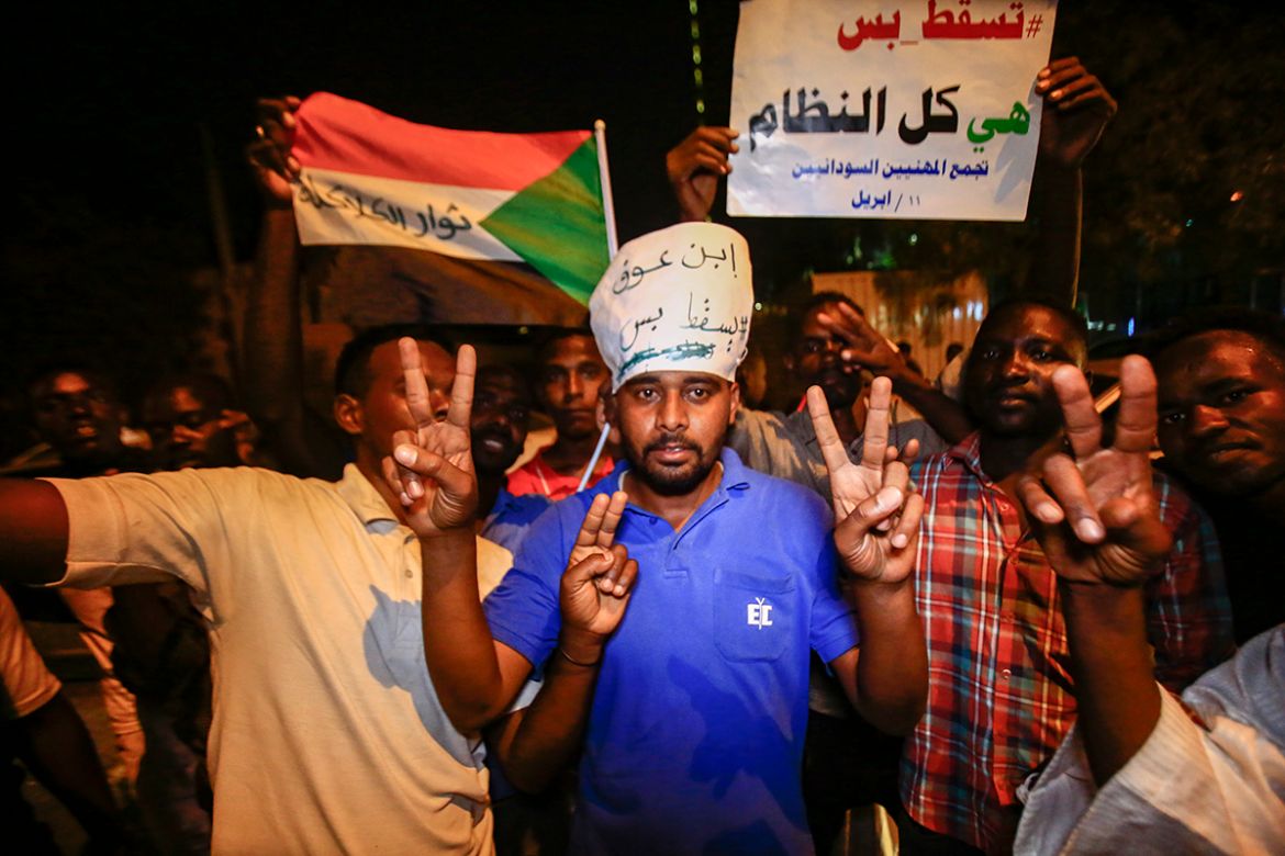 Sudanese protesters flash the victory gesture and raise a sign reading in Arabic "Just fall, that is all, the whole regime", during a demonstration against the new ruling military council put in place