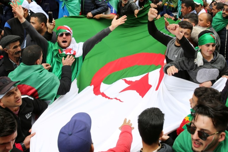 People carry a national flag during a protest to push for the removal of the current political structure, in Algiers