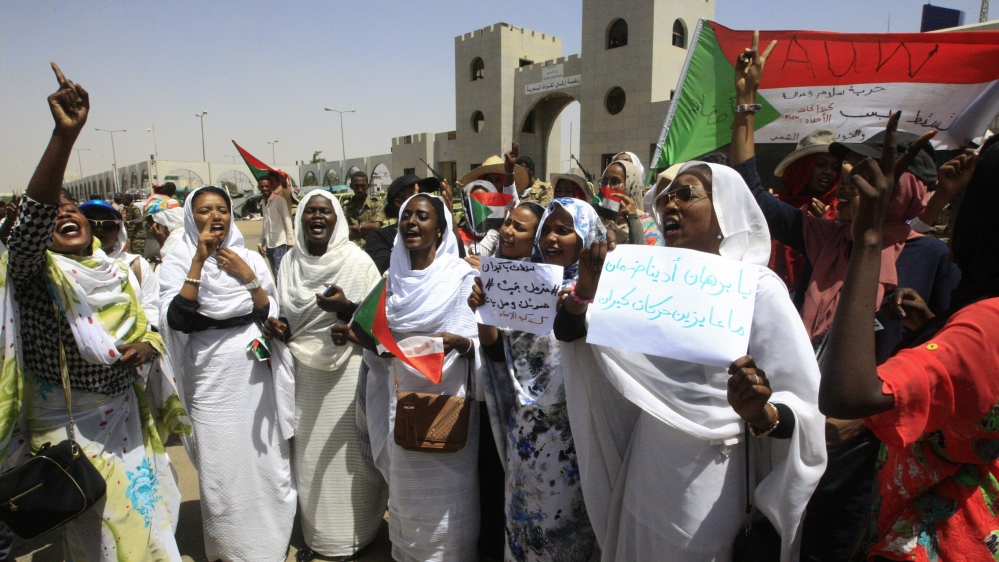 Sudanese women raise banners and a national flag as they rally outside the army headquarters in Khartoum [Ebrahim Hamid/ AFP] 