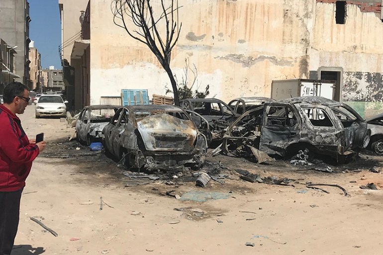 A Libyan man looks at damaged vehicles on April 17, 2019, at the scene of an overnight rocket attack which no group claimed responsibility for so far in the Libyan capital Tripoli. - A number of rocke