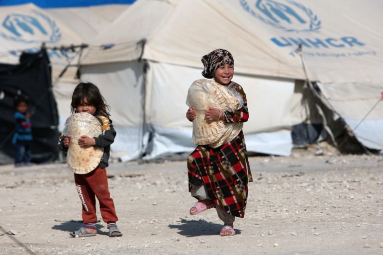 Children holding stacks of bread walk in al-Hol displacement camp in Hasaka governorate