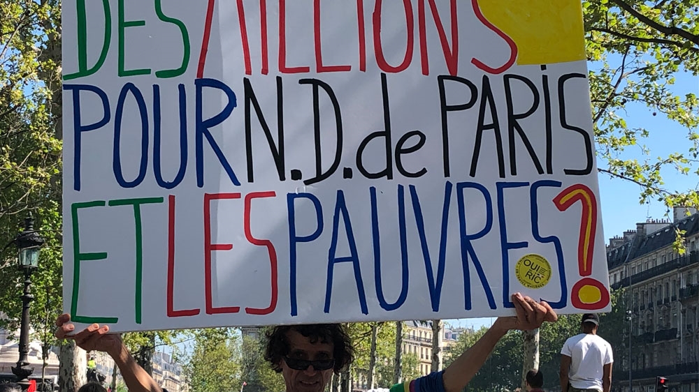 Jean-Baptiste Redde at the Yellow Vest protests in Republique square holds a sign reading 'Millions for Notre Dame - and what about the poor?' [Jabeen Bhatti/Al Jazeera]