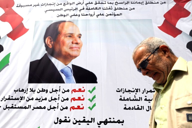 A man walks in front of a banner reading, "Yes to the constitutional amendments, for a better future", with a photo of the Egyptian President Abdel Fattah al-Sisi before