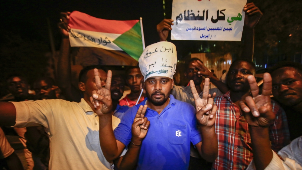 Sudanese protesters flash the victory sign and raise an Arabic poster that reads 'Just fall, that is all, the whole regime' during a demonstration against Sudan's new ruling military council [Ashraf Shazly/AFP]