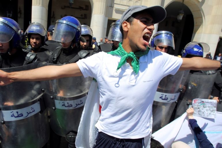 Police members stand guard as a student gestures during an anti government protest in Algiers