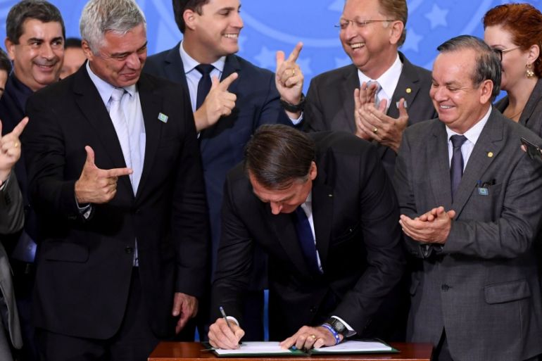 Brazilian President Jair Bolsonaro (C) signs the decree that facilitates to own, carry and import weapons surrounded by parliamentarians during a ceremony at the Planalto Palace in Brasilia, on May 7