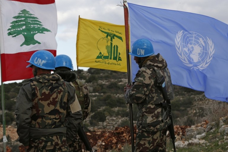 UN peacekeepers hold their flag while standing next to Hezbollah and Lebanese flags, at the site where Israeli excavators are working, near the southern border village of Mays al-Jabal, Lebanon