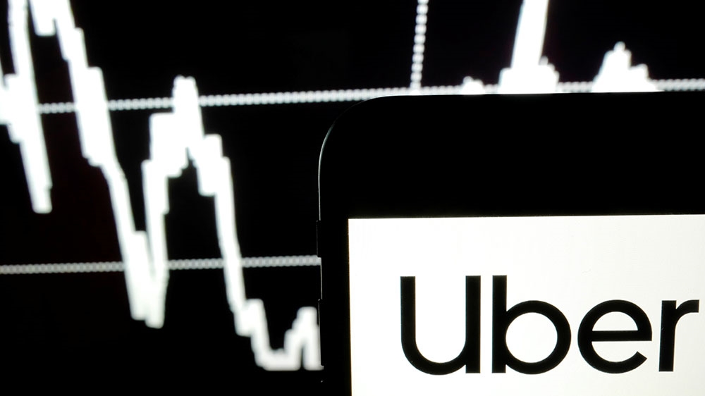 The Uber logo is seen on a smartphone screen as a picture of a stock exchange graph is displayed on a computer screen in this illustration picture [Kacper Pempel/Illustration/Reuters] 