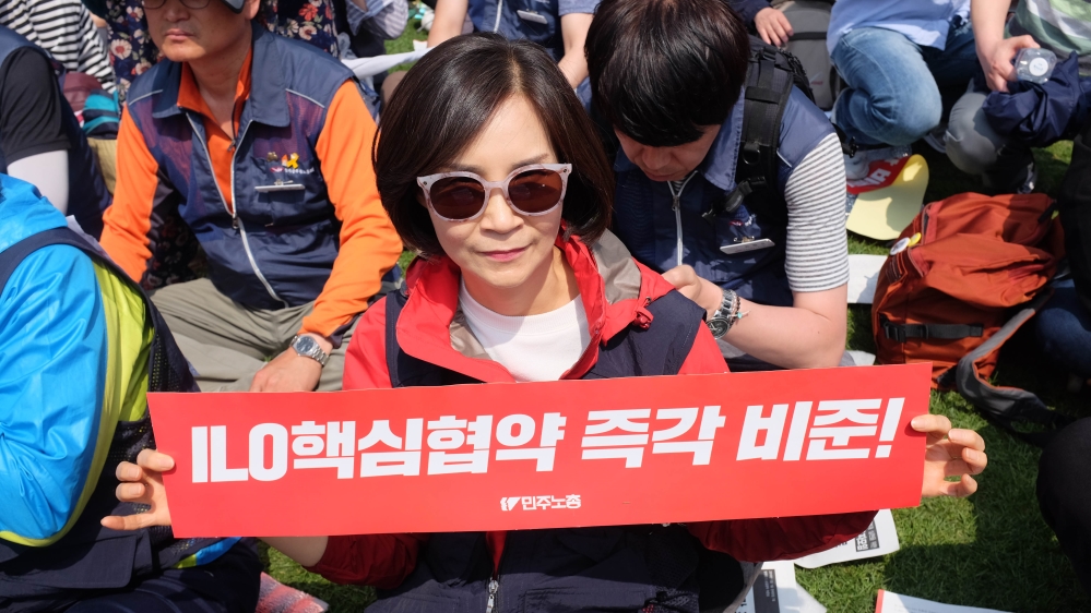 Ko Mun Kyung holds up a banner saying 'immediate ratification of the core ILO conventions' [Sookyoung Lee/Al Jazeera]