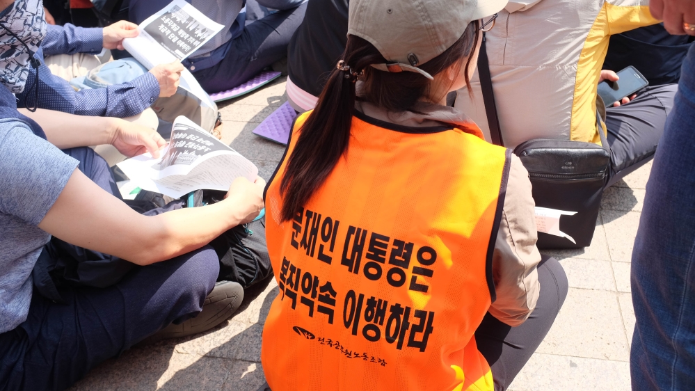 A demonstrator wears an orange vest with 'Moon Jae-in, keep the promise to reinstate' written on it  [Sookyoung Lee/Al Jazeera]