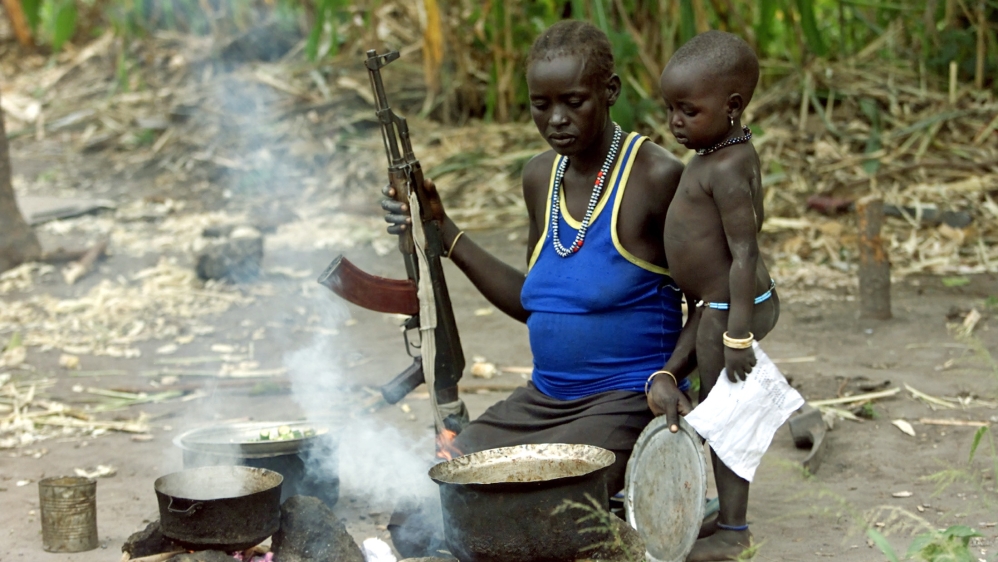 A southern Sudanese woman and her child prepare an evening meal on September 30, 2003, while armed with a Kalashnikov in a homestead in Rumbek, South Sudan [Reuters]