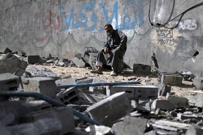 Palestinian man sits on debris near a building that was destroyed by Israeli air strikes, in Gaza City