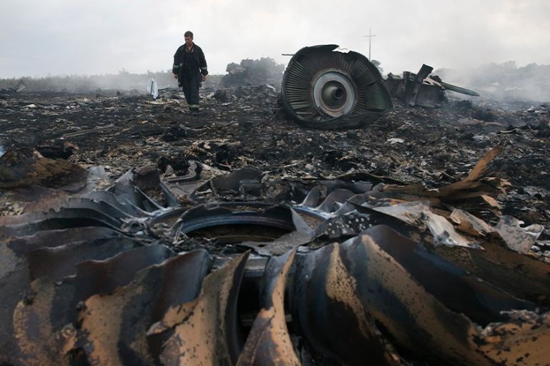 The blackened remains of an aircraft engine and other debris from MH17 in a field in eastern Ukraine. A man is standing in the background