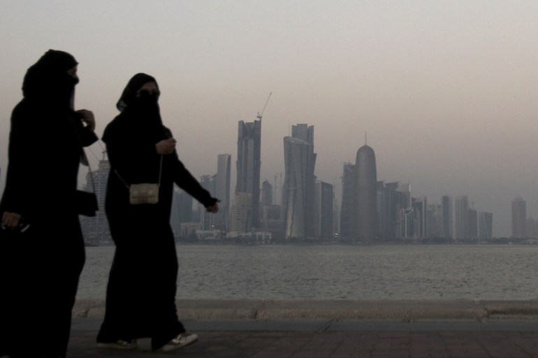 Women walk past buildings as the sun sets in Doha