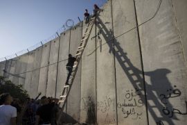Palestinians use a ladder to climb over the separation barrier with Israel on their way to pray at the Al-Aqsa Mosque in Jerusalem, on the Friday of the Muslim holy month of Ramadan, in Al-Ram, north