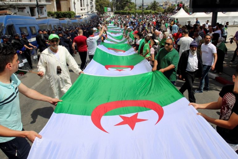 Demonstrators carry a giant national flag during a protest demanding the removal of the ruling elite in Algiers