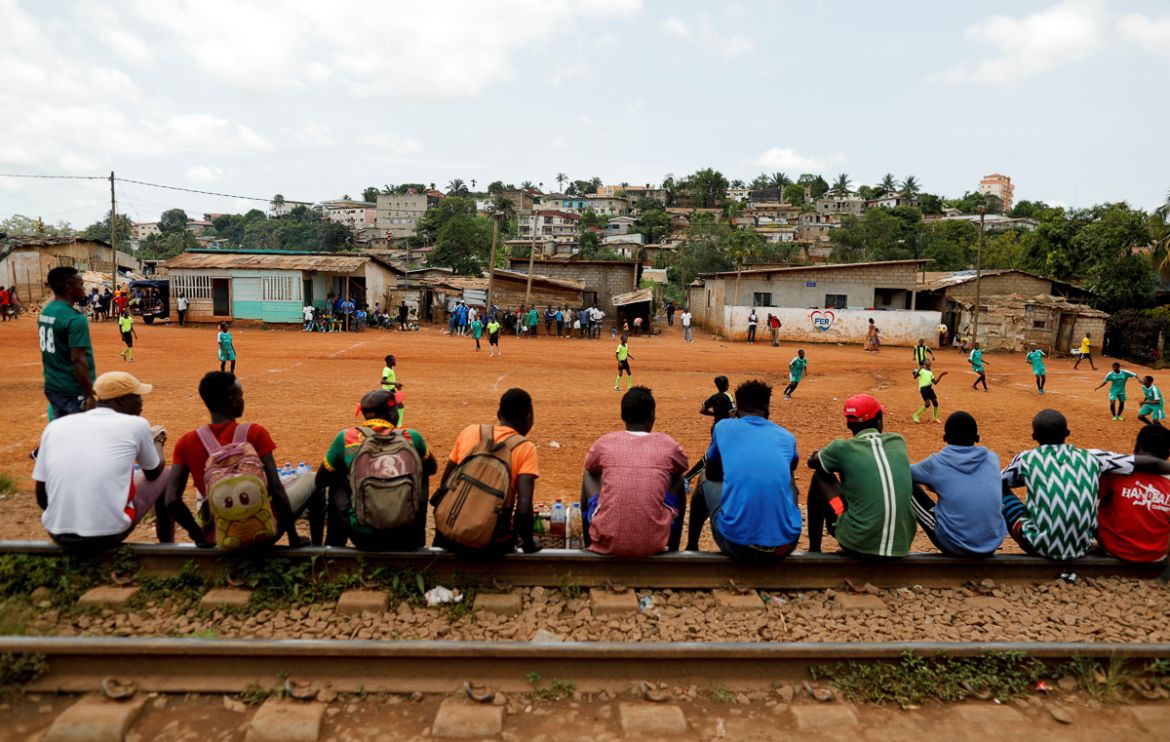 People sit on train tracks as they watch a friendly match between U15, a boys team and U17, a team of first wave of girls being trained by professional coaches of the Rails Foot Academy (RFA), at the