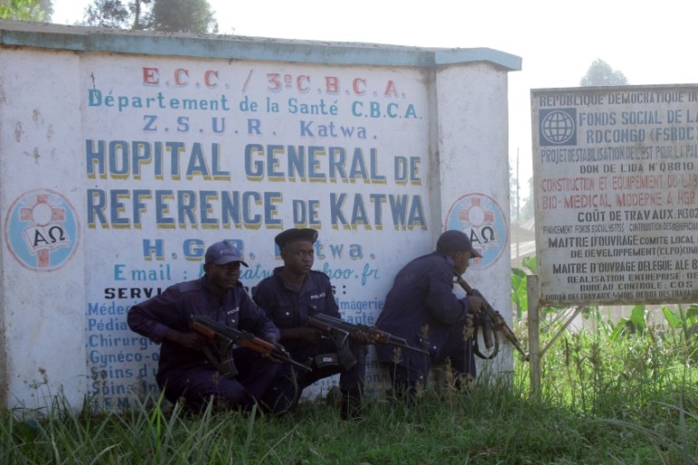 Police shelter behind a hospital sign, as they guard a hospital in Butembo, Congo, on Saturday, April 20, 2019