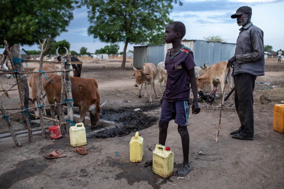 A boy washes a container, while cattle drink from the run-off at a borehole in Thonawai village, Bor county, Jonglei State, South Sudan