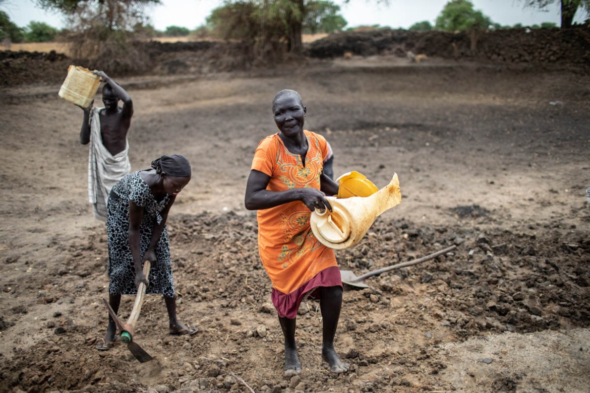 Anyieth Garang (in orange) carries a container of earth out of the pond during a morning of work on April 8, 2019. Anyieth, who lost her husband when the village was attacked during the 2013 conflict,