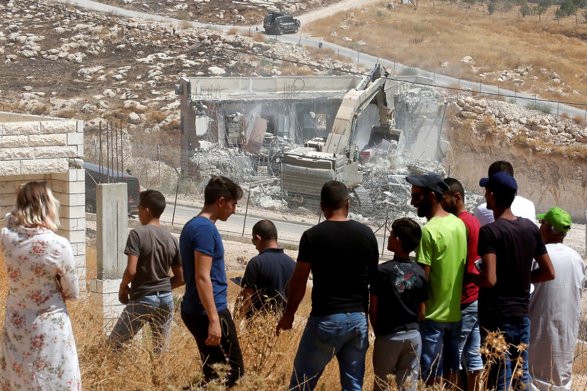 This picture taken from the West Bank on July 22, 2019 shows Palestinians looking at Israeli security forces tearing down one of the Palestinian buildings still under construction which have been issu