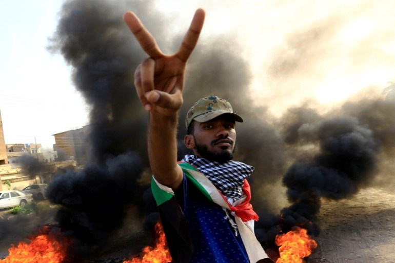 A protester gestures as he burns tyres during a demonstration against a report of the Attorney-General on the dissolution of the sit-in protest in Khartoum