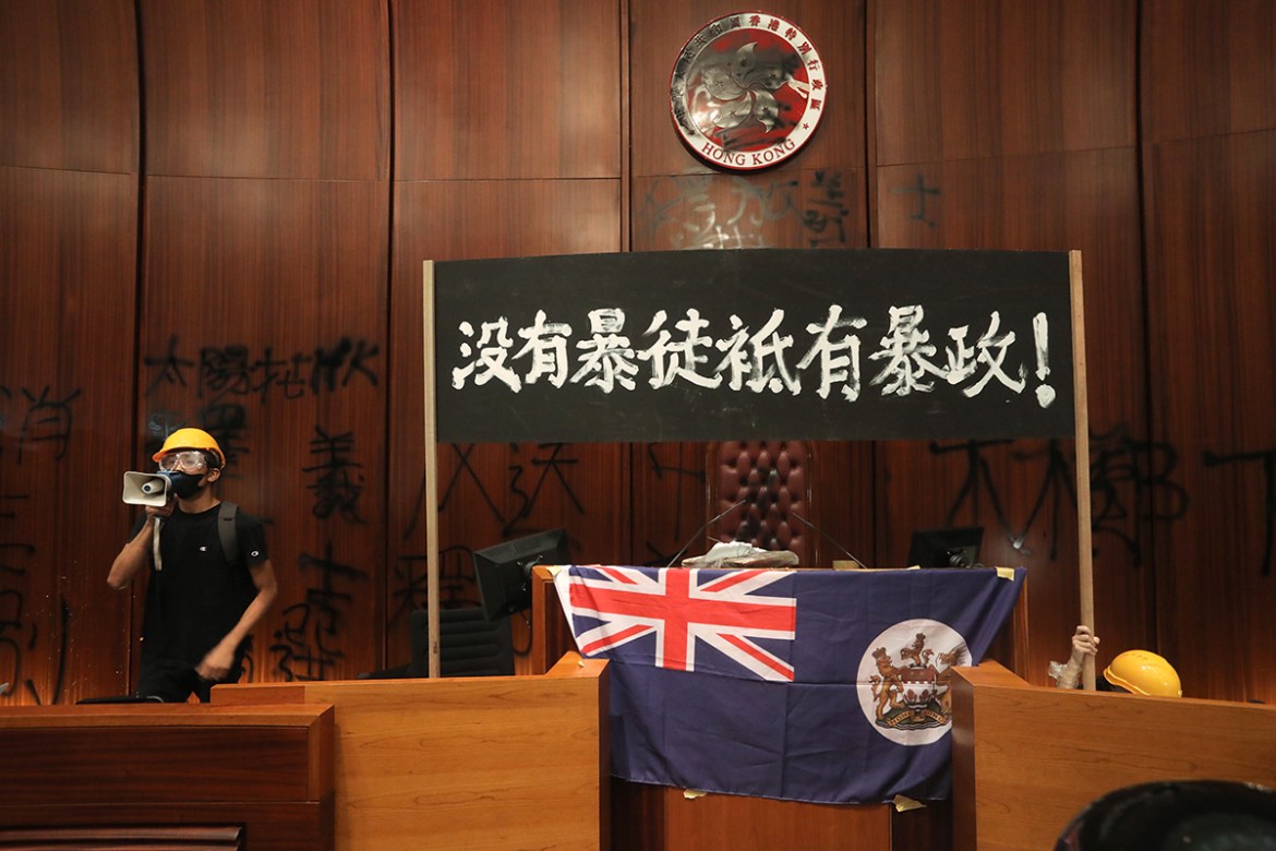 A protester uses a loudspeaker after they broke into the parliament chamber of the government headquarters and tied a British colonial flag to the podium in Hong Kong on July 1, 2019, on the 22nd anni