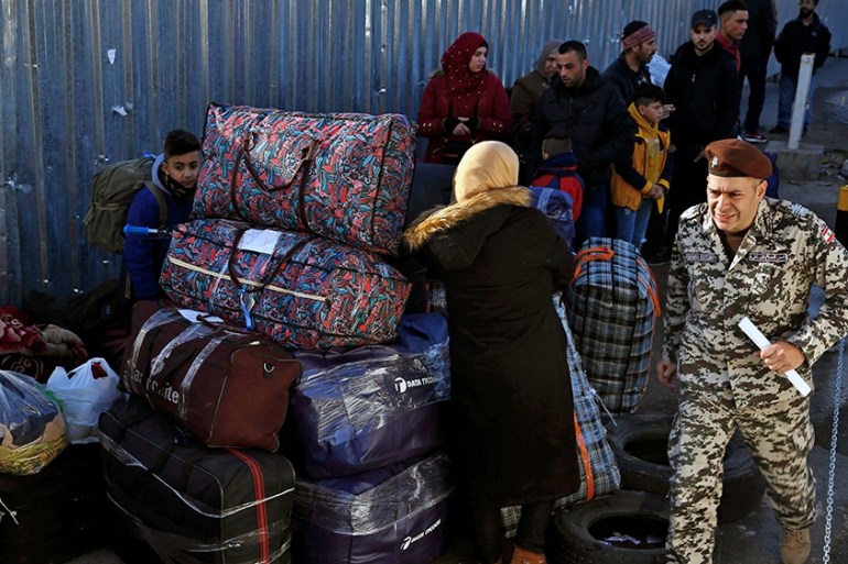 A member of the Lebanese General Security Directorate passes by Syrian refugees gathered with their belongings in northern Beirut suburb of Burj Hammoud, Lebanon, Thursday, Jan. 24, 2019, before headi